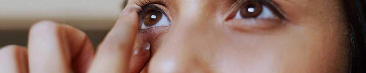 Et nærbillede af en ung kvinde, der kigger ind i et spejl og tager sine kontaktlinser på.